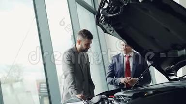 专业的汽车推销员在汽车引擎盖下演示客户汽车发动机，男人们正在寻找汽车零部件